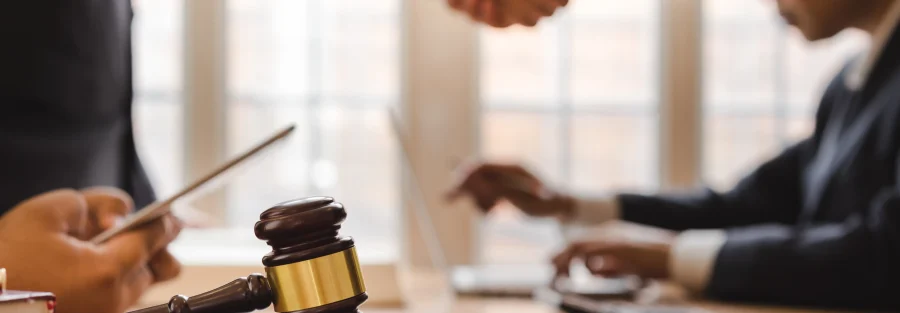 This image shows a close-up of a gavel resting on a table, symbolizing a legal setting, while two individuals in business attire shake hands in the background. The scene conveys a sense of agreement or negotiation, with other participants focusing on documents and technology around them. The image suggests a legal or professional context, possibly related to water rights in Idaho, with the handshake representing the resolution of a legal matter or contract involving these rights.